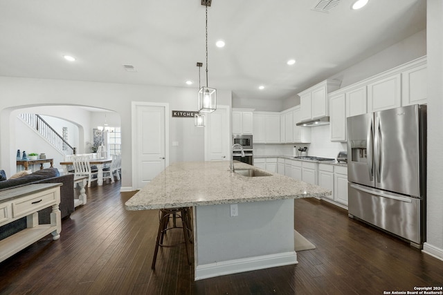 kitchen featuring dark hardwood / wood-style floors, appliances with stainless steel finishes, light stone counters, sink, and a center island with sink