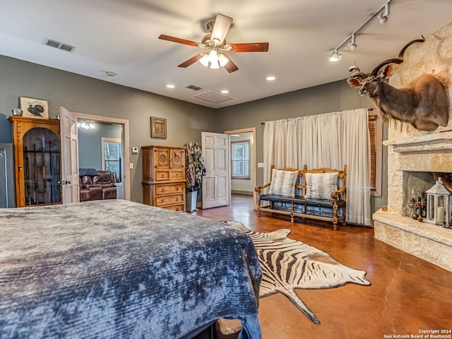 bedroom featuring ceiling fan, rail lighting, and a stone fireplace