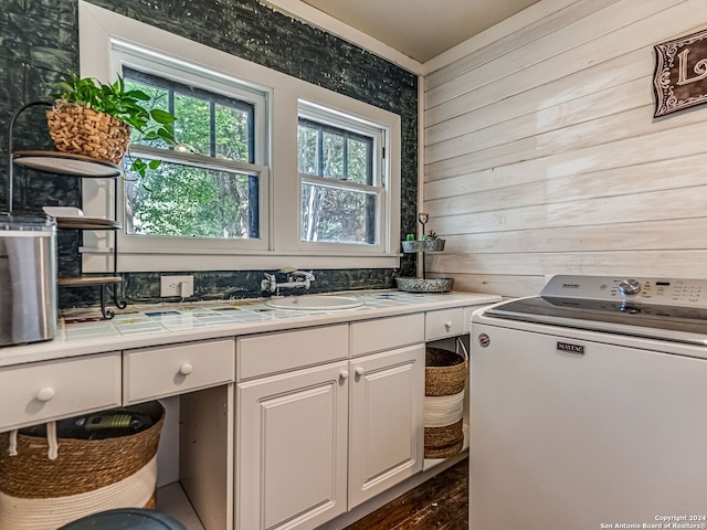 kitchen featuring sink, white cabinets, washer / dryer, and wood walls