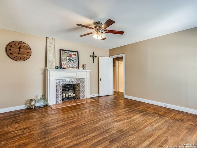 unfurnished living room with ceiling fan, a tiled fireplace, and wood-type flooring