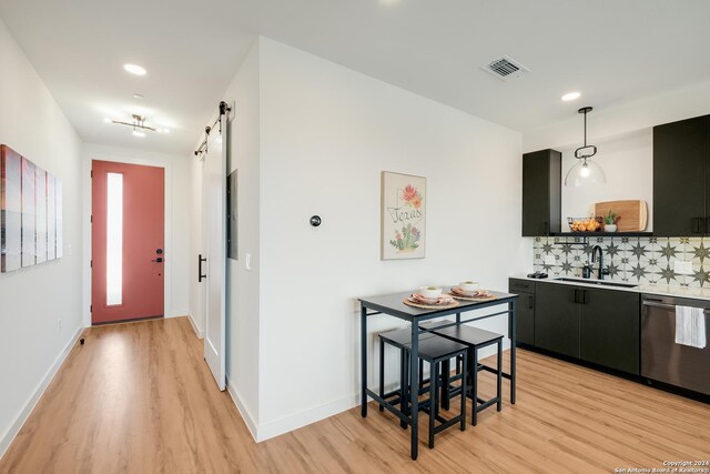 kitchen featuring light wood-type flooring, decorative backsplash, stainless steel dishwasher, sink, and decorative light fixtures