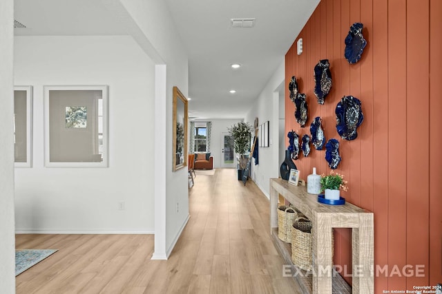 corridor with light hardwood / wood-style floors and wood walls