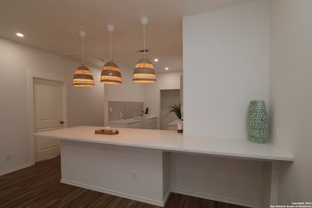 kitchen with kitchen peninsula, dark wood-type flooring, a kitchen bar, and hanging light fixtures