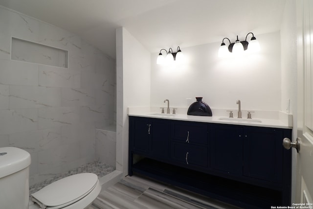 bathroom with toilet, a tile shower, and vanity