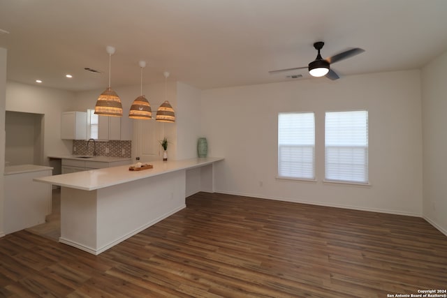 kitchen with kitchen peninsula, tasteful backsplash, hanging light fixtures, and dark wood-type flooring