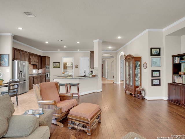 living room featuring sink, crown molding, light hardwood / wood-style floors, and ornate columns