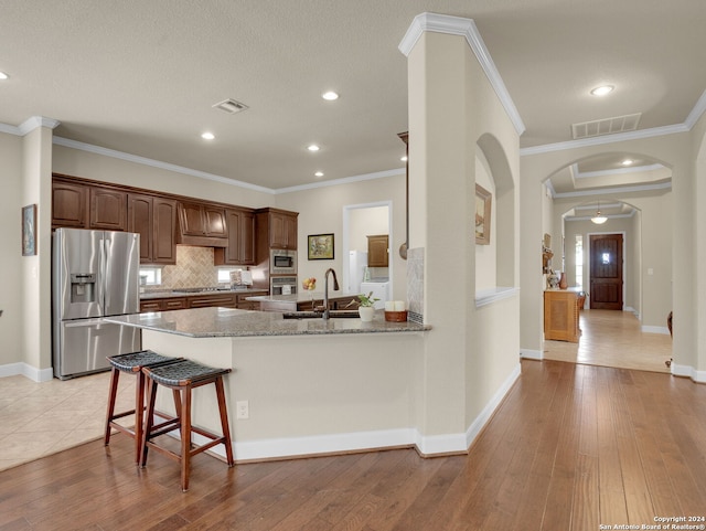 kitchen with light wood-type flooring, a kitchen bar, kitchen peninsula, crown molding, and stainless steel appliances