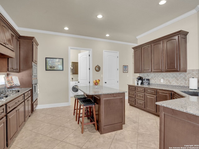 kitchen with washer / clothes dryer, appliances with stainless steel finishes, light stone countertops, and crown molding