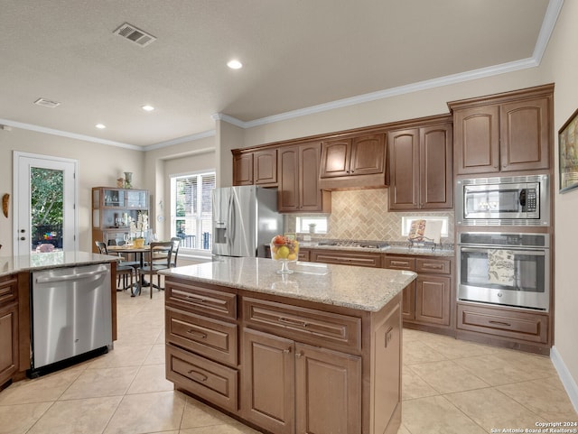 kitchen with light stone counters, stainless steel appliances, ornamental molding, decorative backsplash, and a center island