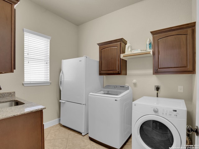 clothes washing area featuring sink, light tile patterned floors, cabinets, and washer and dryer