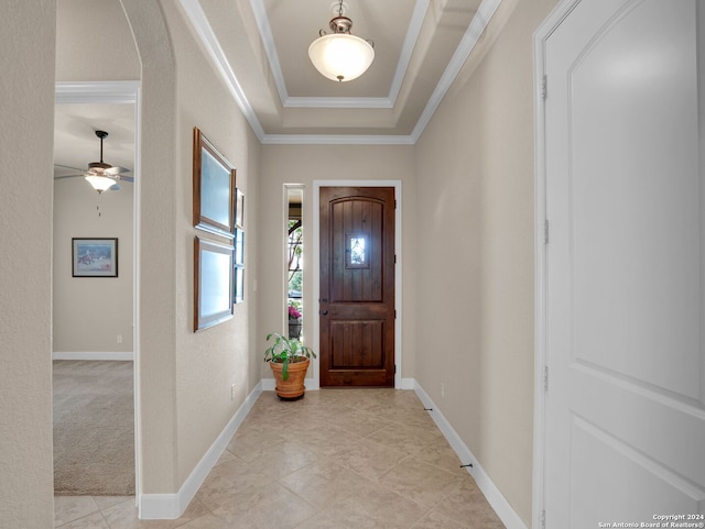 foyer entrance featuring arched walkways, ceiling fan, baseboards, a tray ceiling, and crown molding