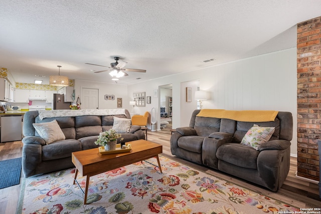 living room featuring ceiling fan, a textured ceiling, light hardwood / wood-style flooring, and brick wall