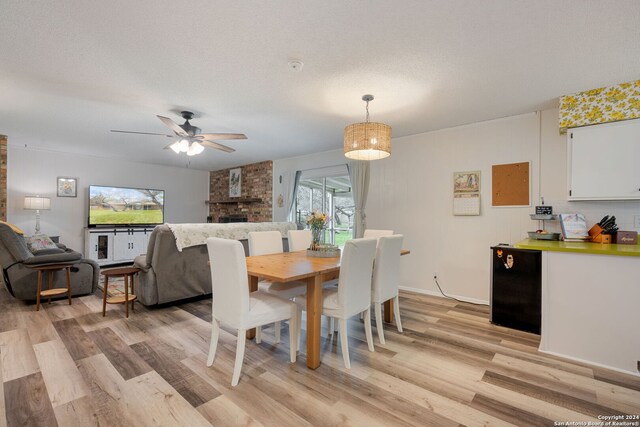 dining room with light wood-type flooring, a brick fireplace, and ceiling fan