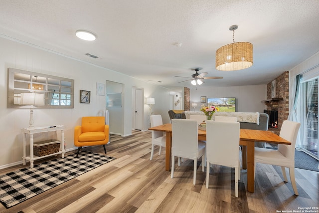 dining area featuring ceiling fan, a large fireplace, wood-type flooring, and a textured ceiling