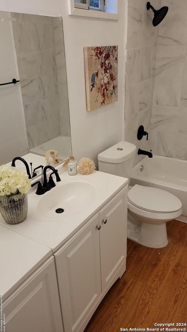 full bathroom featuring hardwood / wood-style flooring, vanity, tiled shower / bath combo, and toilet