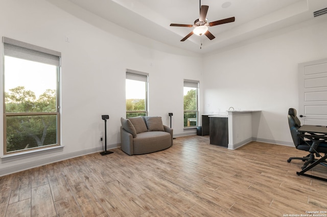 office space featuring ceiling fan, a high ceiling, light hardwood / wood-style flooring, and a tray ceiling