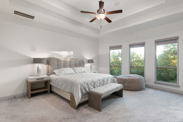 bedroom featuring ceiling fan, light colored carpet, and a tray ceiling