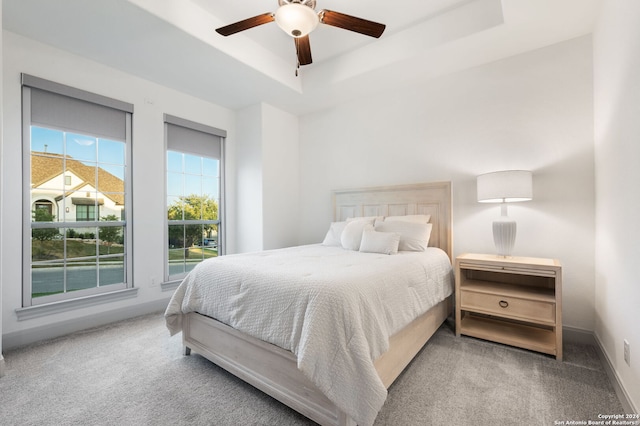 carpeted bedroom with ceiling fan and a tray ceiling