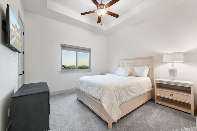 carpeted bedroom with ceiling fan and a raised ceiling