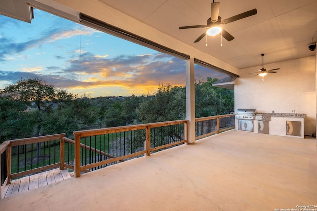 patio terrace at dusk featuring ceiling fan, area for grilling, and an outdoor kitchen