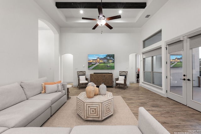 living room featuring a high ceiling, beam ceiling, hardwood / wood-style flooring, french doors, and a raised ceiling