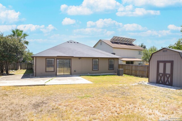 back of property featuring cooling unit, a patio, a lawn, and a storage unit