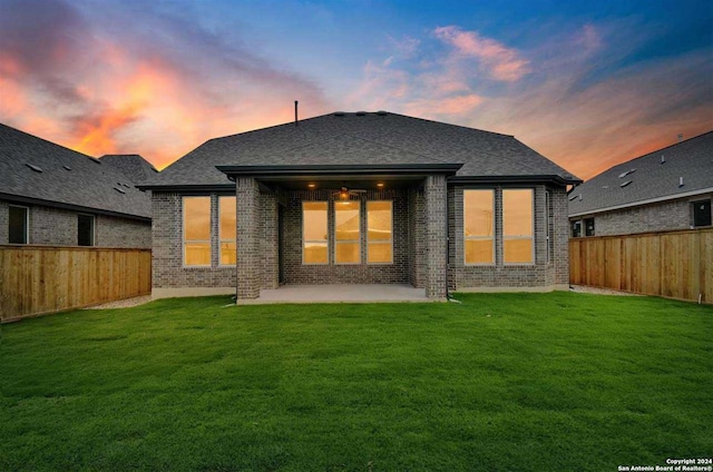 back house at dusk featuring a patio area and a yard