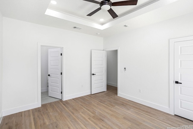 unfurnished bedroom with ceiling fan, connected bathroom, light hardwood / wood-style flooring, and a tray ceiling