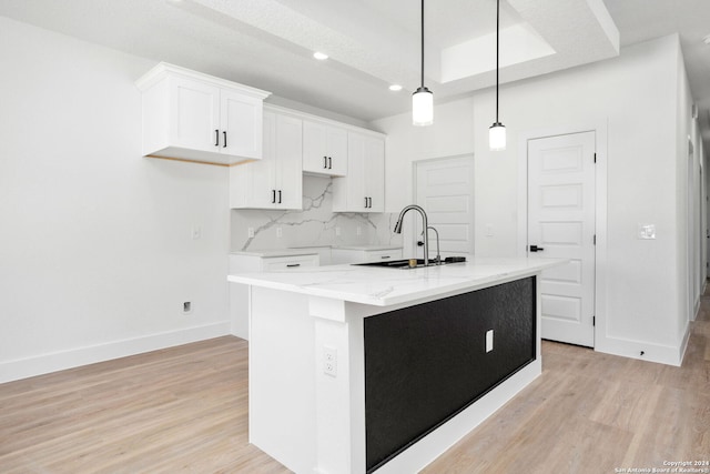 kitchen with backsplash, a center island with sink, light hardwood / wood-style floors, and light stone counters