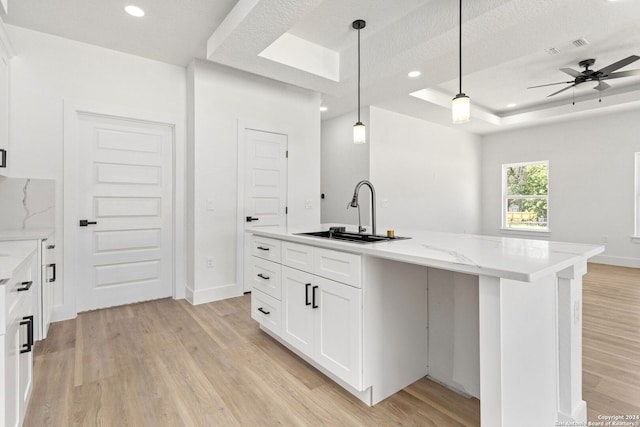 kitchen featuring sink, an island with sink, light wood-type flooring, a tray ceiling, and ceiling fan