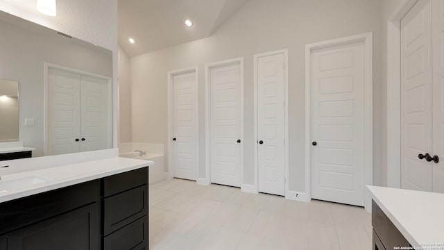 bathroom featuring tile patterned flooring, vaulted ceiling, a washtub, and vanity