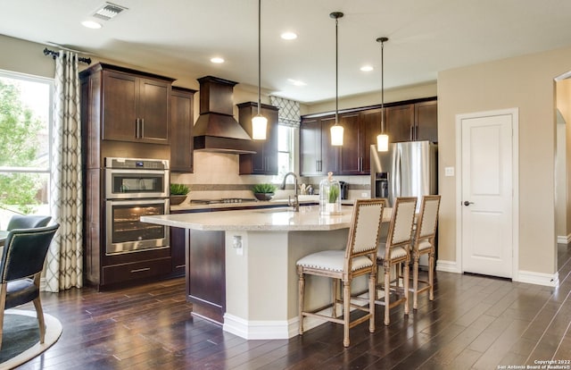 kitchen featuring a center island with sink, visible vents, hanging light fixtures, custom exhaust hood, and stainless steel appliances