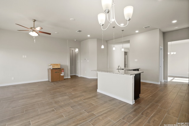 kitchen featuring sink, an island with sink, ceiling fan with notable chandelier, light stone countertops, and pendant lighting