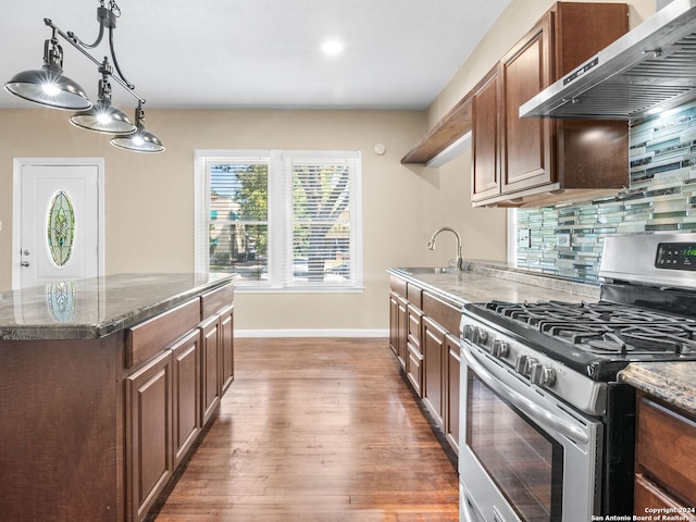 kitchen featuring stainless steel gas stove, dark stone counters, light hardwood / wood-style flooring, backsplash, and wall chimney exhaust hood