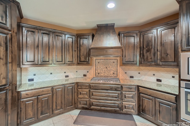 kitchen featuring custom exhaust hood, light stone counters, light tile patterned floors, and decorative backsplash