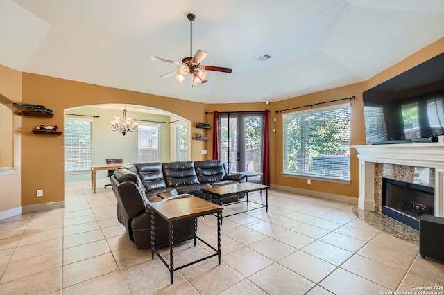 tiled living room featuring ceiling fan with notable chandelier, a fireplace, and vaulted ceiling