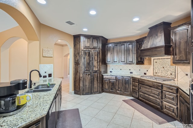 kitchen featuring stainless steel gas stovetop, custom exhaust hood, light stone countertops, and dark brown cabinets