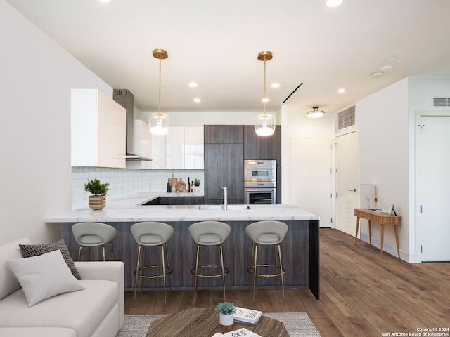 kitchen featuring white cabinets, kitchen peninsula, dark hardwood / wood-style flooring, decorative light fixtures, and wall chimney range hood