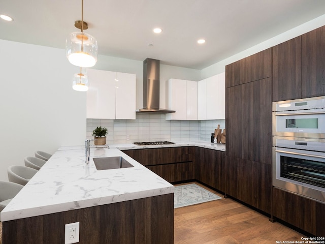 kitchen featuring white cabinets, backsplash, pendant lighting, light hardwood / wood-style flooring, and wall chimney range hood