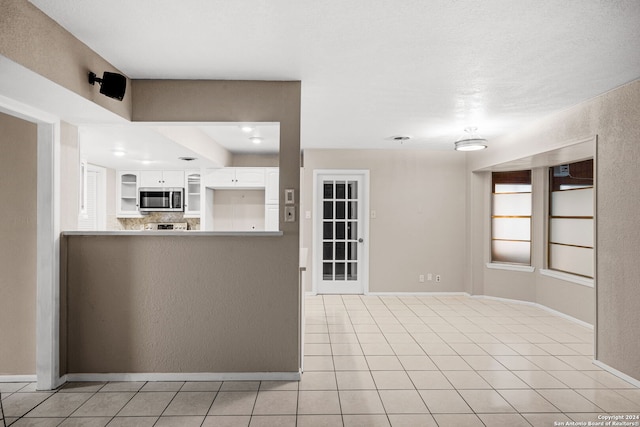 kitchen with light tile patterned floors, a peninsula, white cabinetry, light countertops, and stainless steel microwave