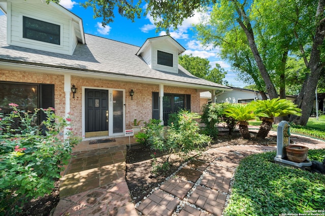 view of front facade featuring covered porch, a shingled roof, and brick siding