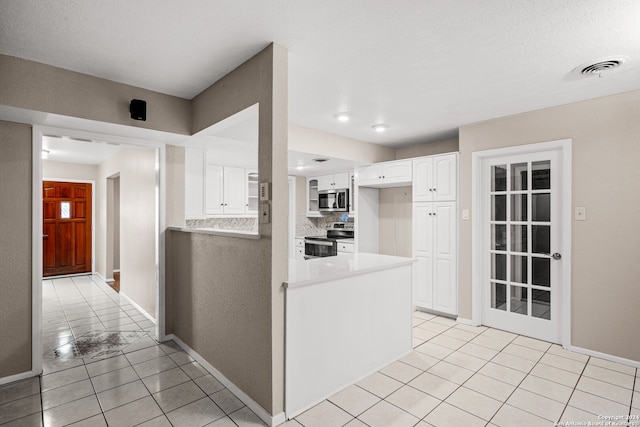 kitchen with stainless steel appliances, light tile patterned floors, backsplash, kitchen peninsula, and white cabinets