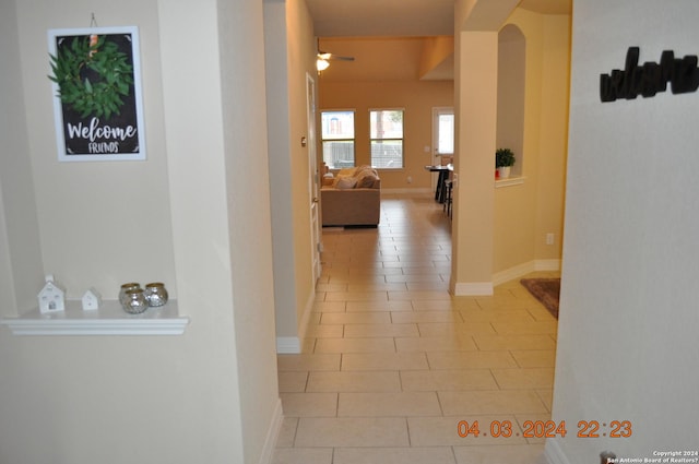 hall with light tile patterned floors, baseboards, and arched walkways