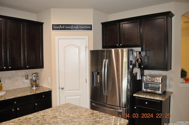 kitchen featuring tasteful backsplash, dark brown cabinetry, stainless steel refrigerator with ice dispenser, and light stone countertops