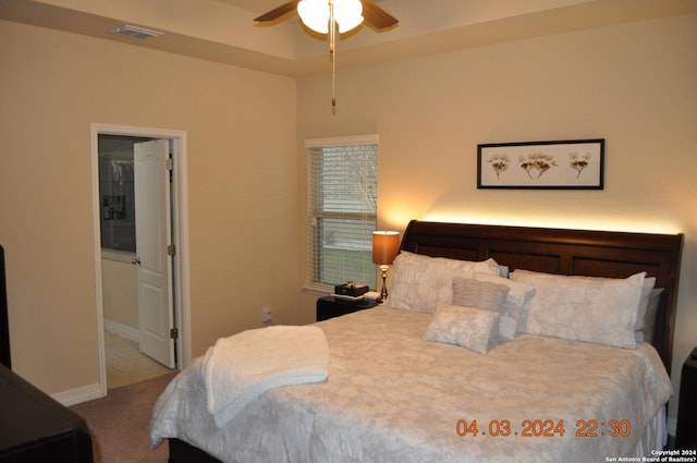 bedroom with light carpet, visible vents, baseboards, ensuite bath, and a tray ceiling