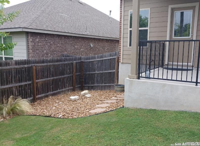 view of side of home featuring brick siding, roof with shingles, fence private yard, and a lawn