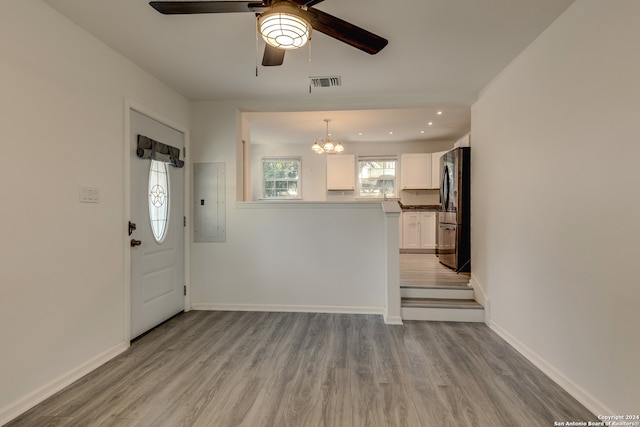 foyer with light wood-type flooring, ceiling fan with notable chandelier, and electric panel