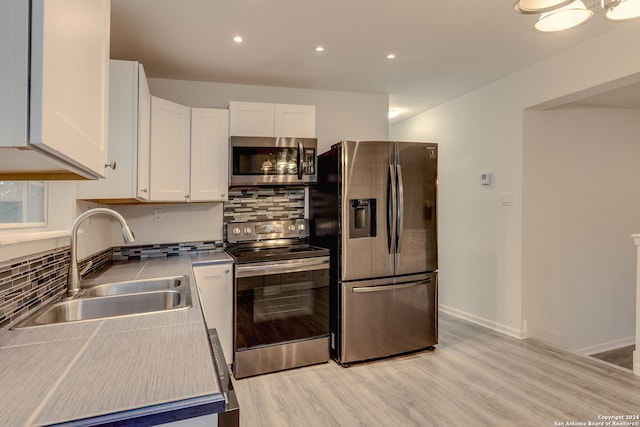 kitchen featuring appliances with stainless steel finishes, decorative backsplash, sink, light wood-type flooring, and white cabinets