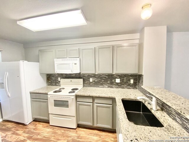 kitchen with sink, white appliances, light wood-type flooring, and tasteful backsplash