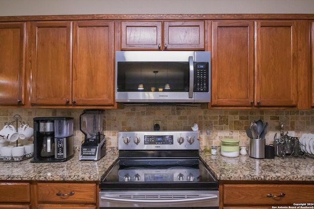 kitchen featuring appliances with stainless steel finishes, brown cabinetry, backsplash, and light stone counters